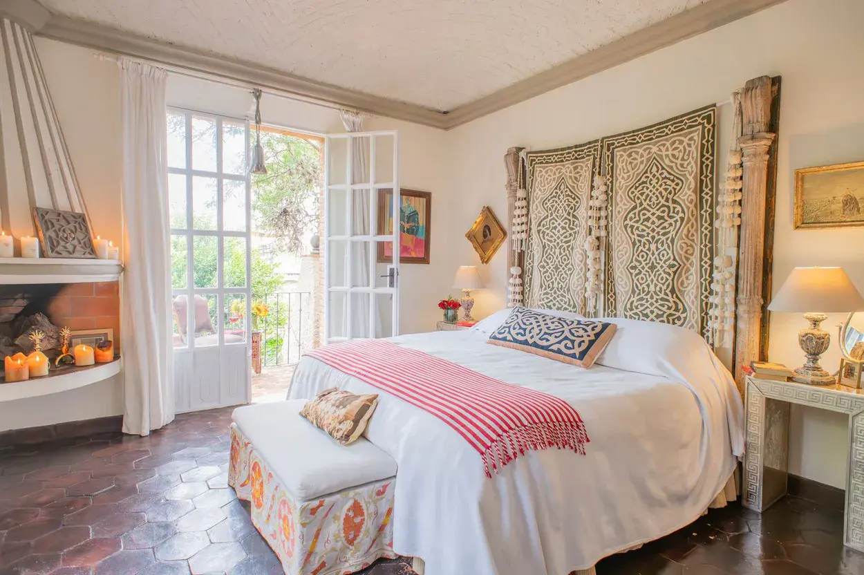 Casa Kate, primary bedroom with a carved wood headboard and a corner fireplace, San Miguel de Allende