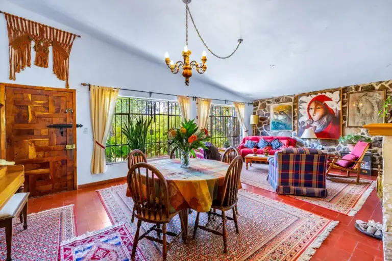 Casa La Chiquita, open living and dining room with a round dining table, plaid sofas, a red couch and a carved wood door, San Miguel de Allende