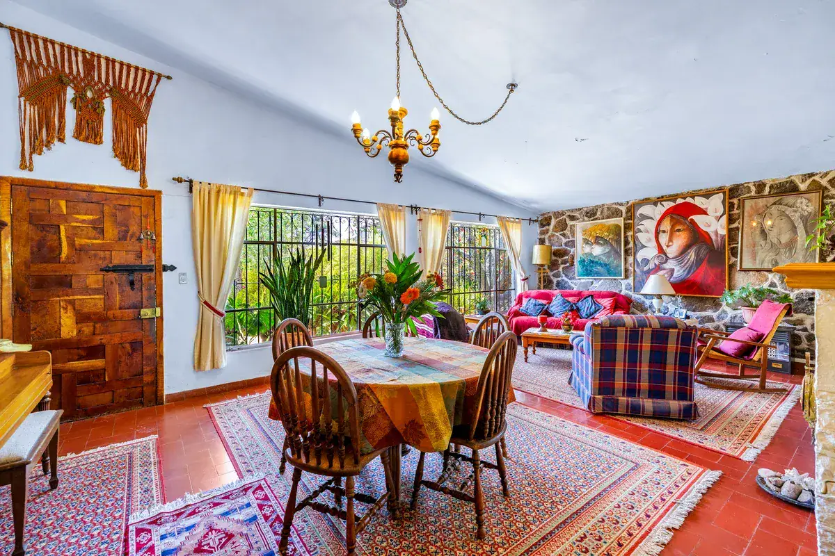 Casa La Chiquita, open living and dining room with a round dining table, plaid sofas, a red couch and a carved wood door, San Miguel de Allende