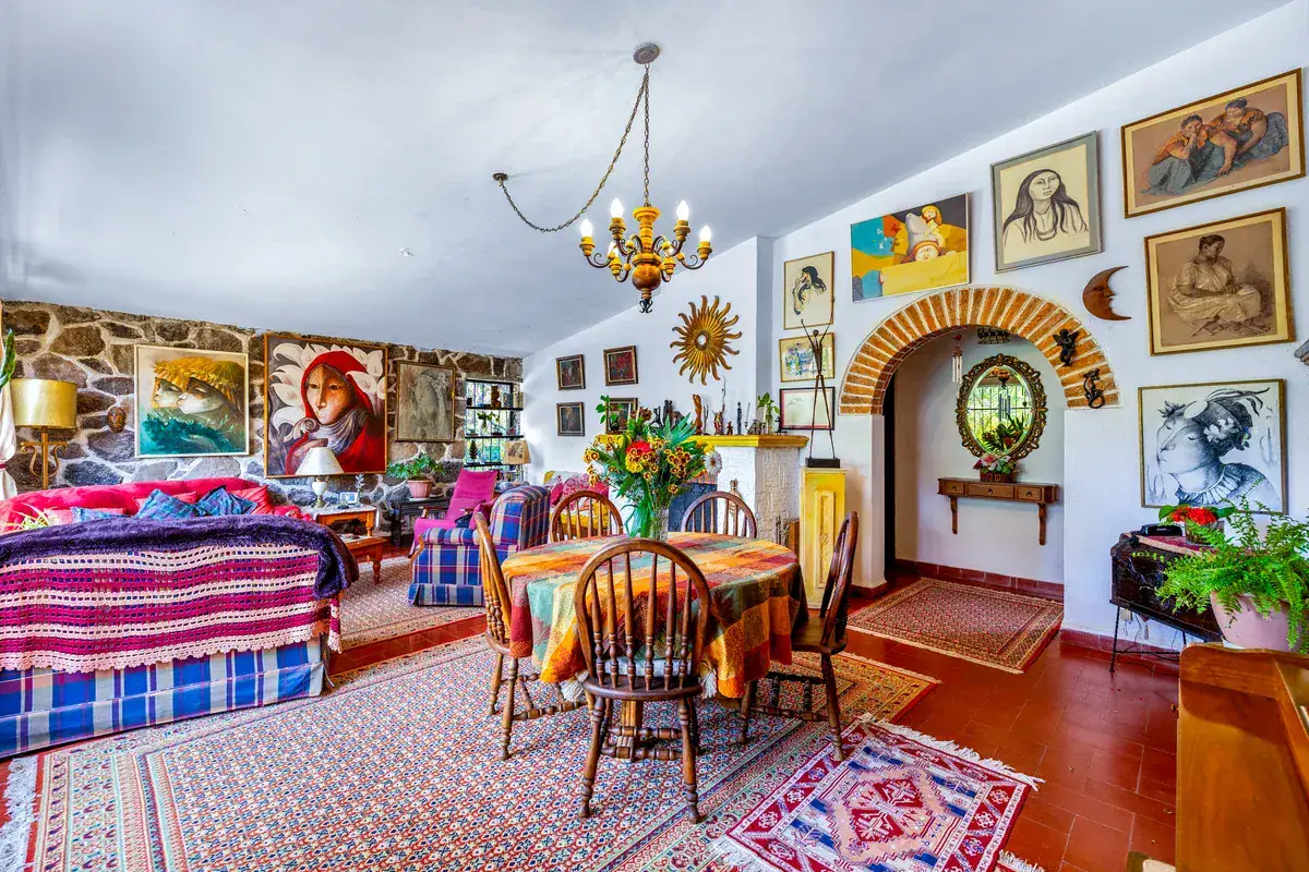 Casa La Chiquita, living room with a stone-arched doorway, framed art covering the wall, a dining table and a plaid sofa, San Miguel de Allende