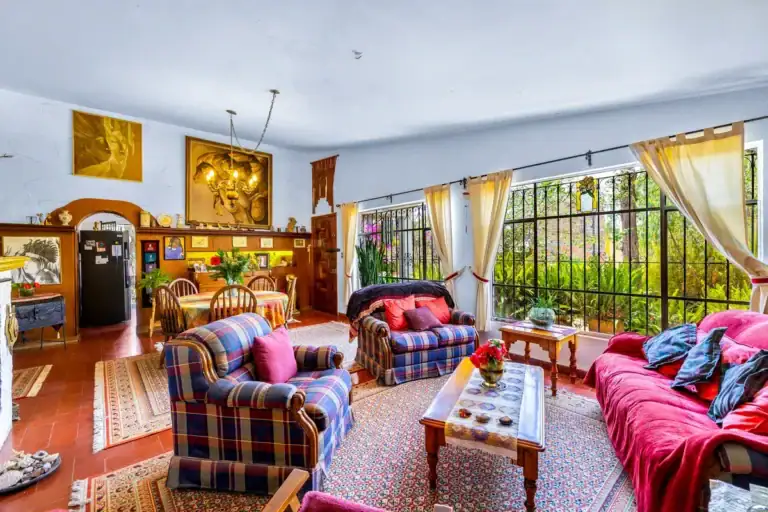 Casa La Chiquita, living and dining room with plaid armchairs, a red sofa, a coffee table and barred windows to the garden, San Miguel de Allende