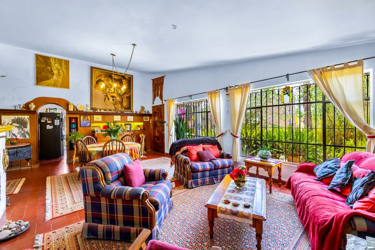 Casa La Chiquita, living and dining room with plaid armchairs, a red sofa, a coffee table and barred windows to the garden, San Miguel de Allende