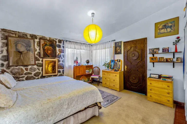 Casa La Chiquita, bedroom with a stone wall, framed paintings, a double bed and a carved wood door, San Miguel de Allende