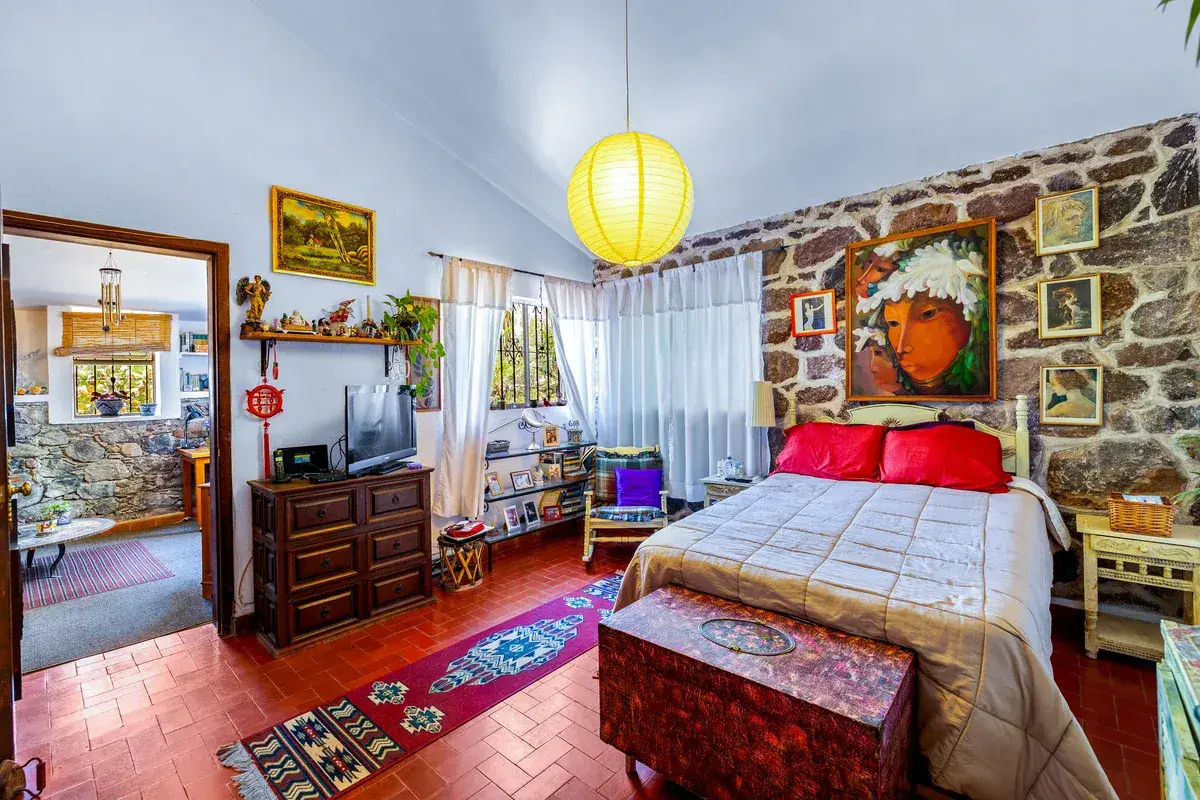 Casa La Chiquita, bedroom with a stone wall, a red cushion bed, a dark wood dresser and a television, San Miguel de Allende