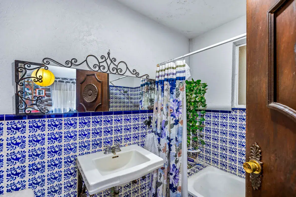 Casa La Chiquita, bathroom with blue and white tile, a pedestal sink, a floral shower curtain and an ornate mirror, San Miguel de Allende