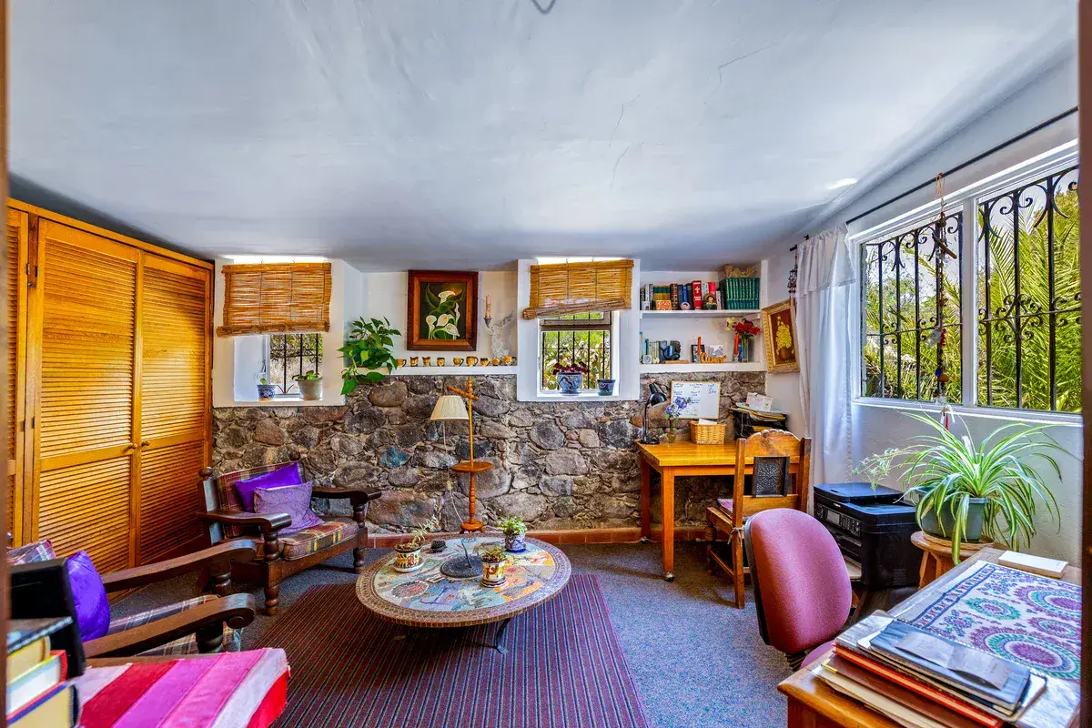 Casa La Chiquita, study with wood louvered closets, a stone wall, a wood desk, a round mosaic table and shelves, San Miguel de Allende