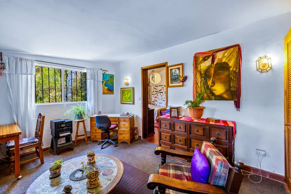 Casa La Chiquita, study with a wood chest of drawers, a desk and chair, a round mosaic table and a framed portrait, San Miguel de Allende