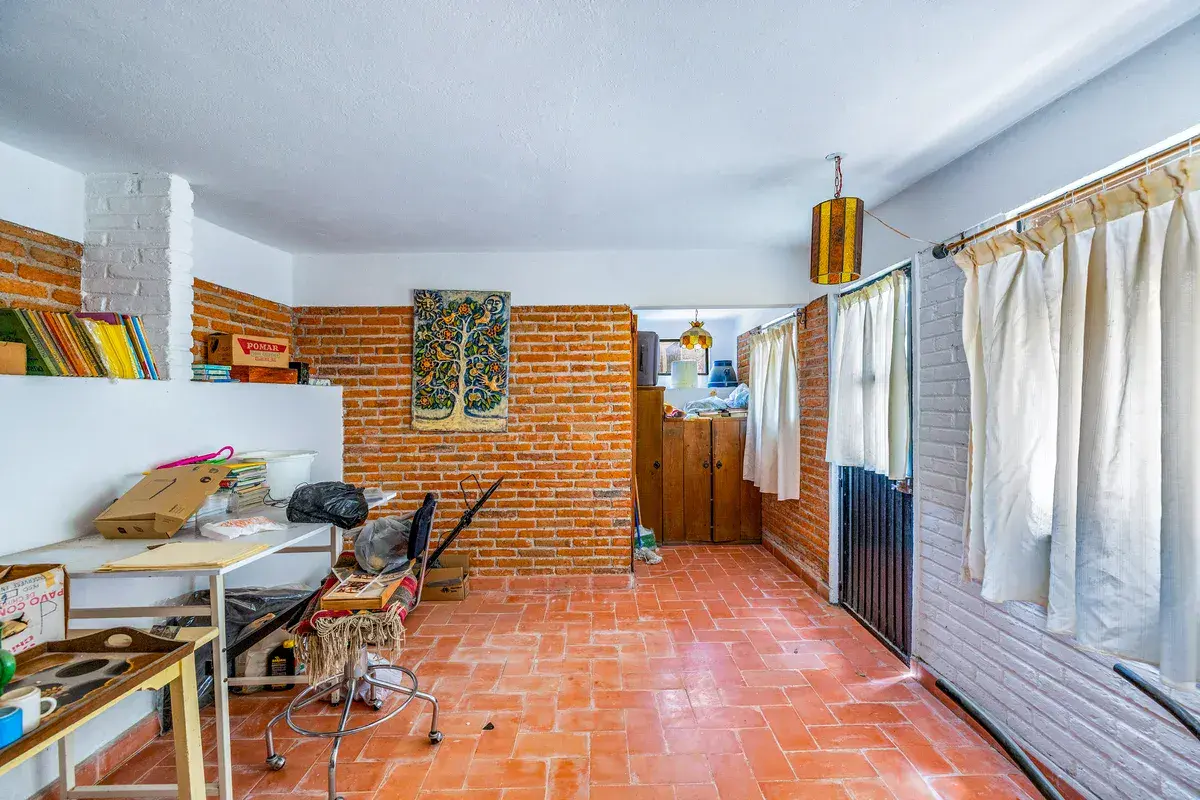 Casa La Chiquita, brick-walled room with a terracotta floor, a work table, shelves and curtained windows, San Miguel de Allende