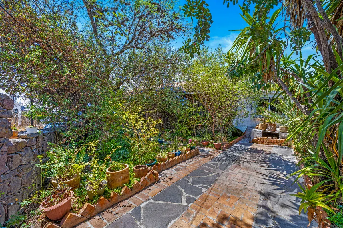 Casa La Chiquita, garden path of flagstones and brick beside planted pots and a stone wall, San Miguel de Allende