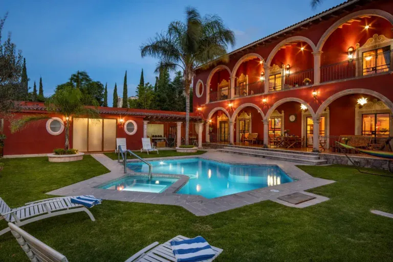 Casa La Colina, red arcaded house with a lit pool and lawn at dusk, San Miguel de Allende