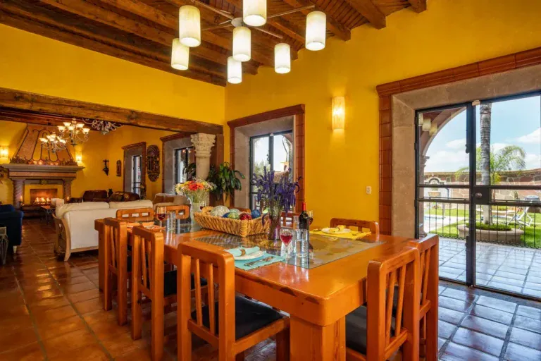 Casa La Colina, yellow dining and living room with a long wood table and a fireplace, San Miguel de Allende