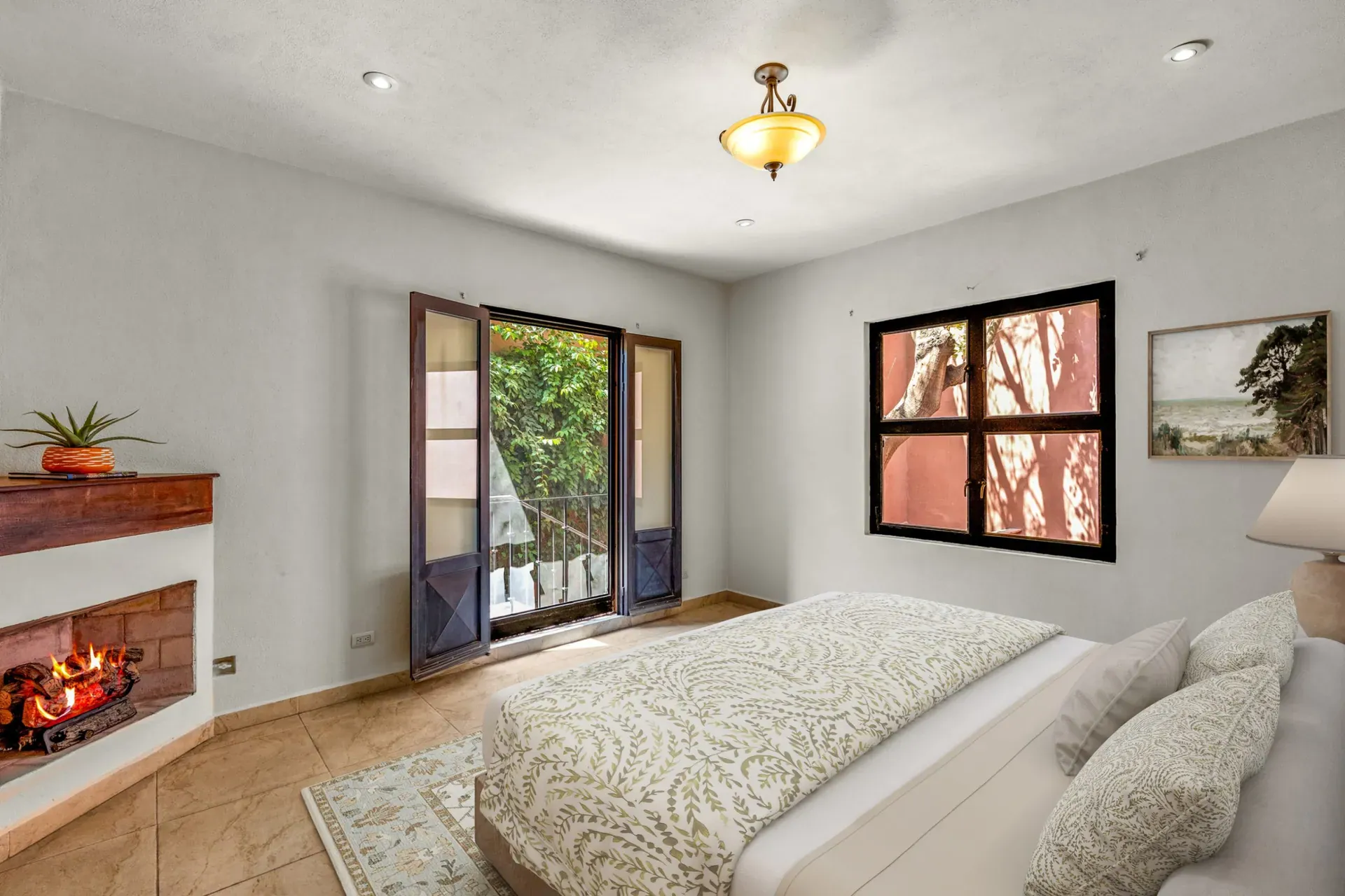 Casa Las Monjas, bedroom with a patterned bedspread, a corner fireplace and a window with a black frame (virtually staged), San Miguel de Allende