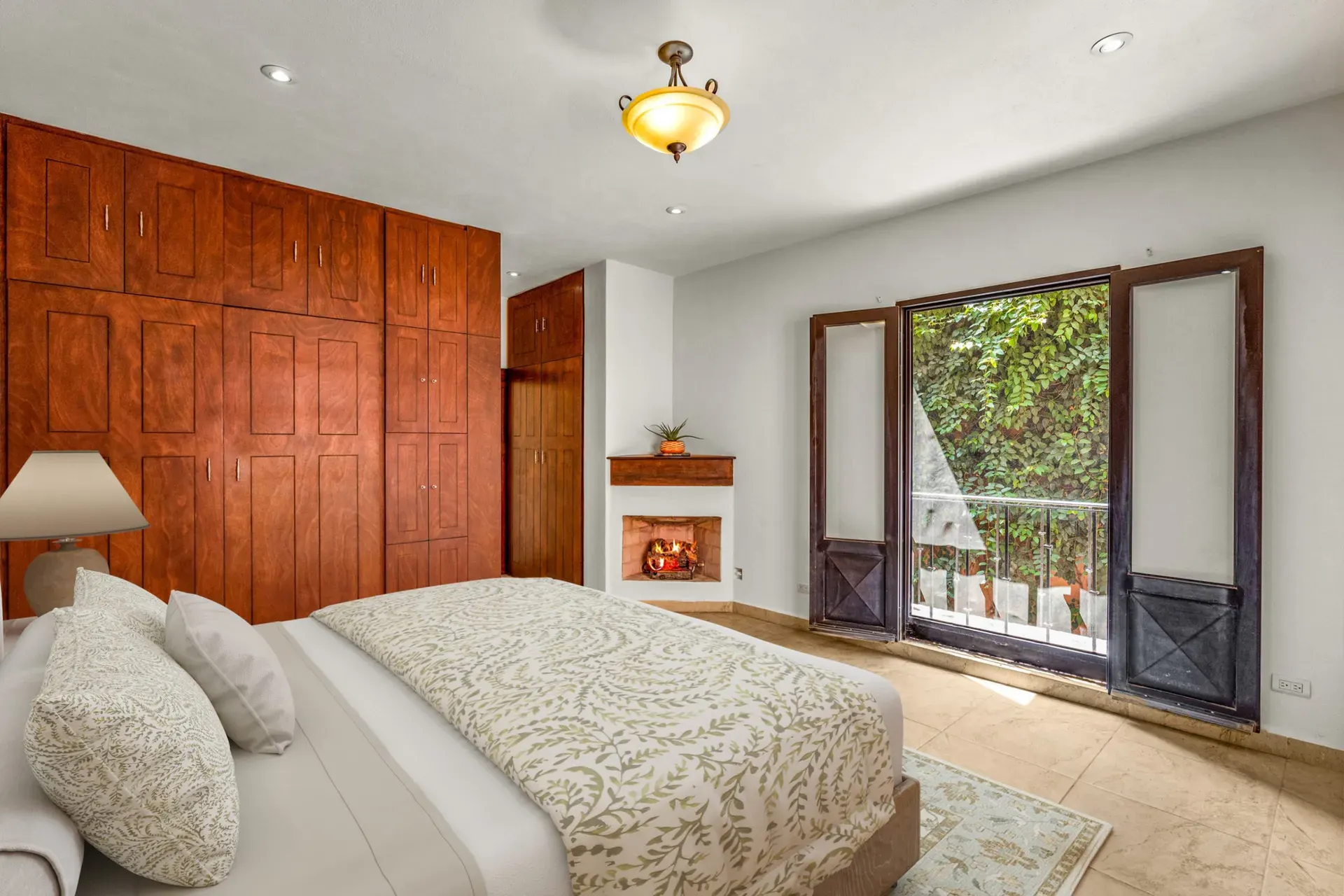 Casa Las Monjas, bedroom with a patterned bedspread, a wall of wood wardrobes and a balcony door (virtually staged), San Miguel de Allende