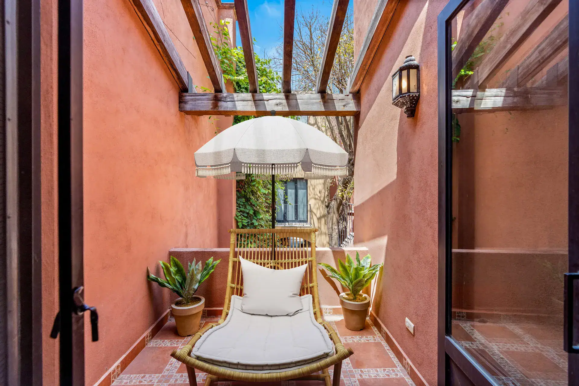 Casa Las Monjas, narrow terracotta courtyard with a lounge chair, a fringed umbrella, potted plants and a pergola, San Miguel de Allende