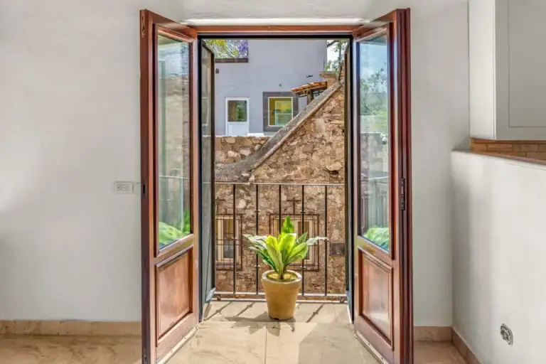 Casa Las Monjas, French doors opening to a small balcony with a potted plant and an old stone wall, San Miguel de Allende