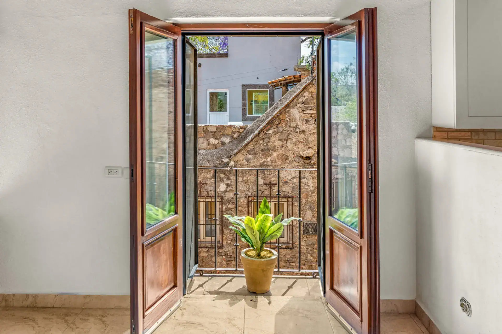 Casa Las Monjas, French doors opening to a small balcony with a potted plant and an old stone wall, San Miguel de Allende