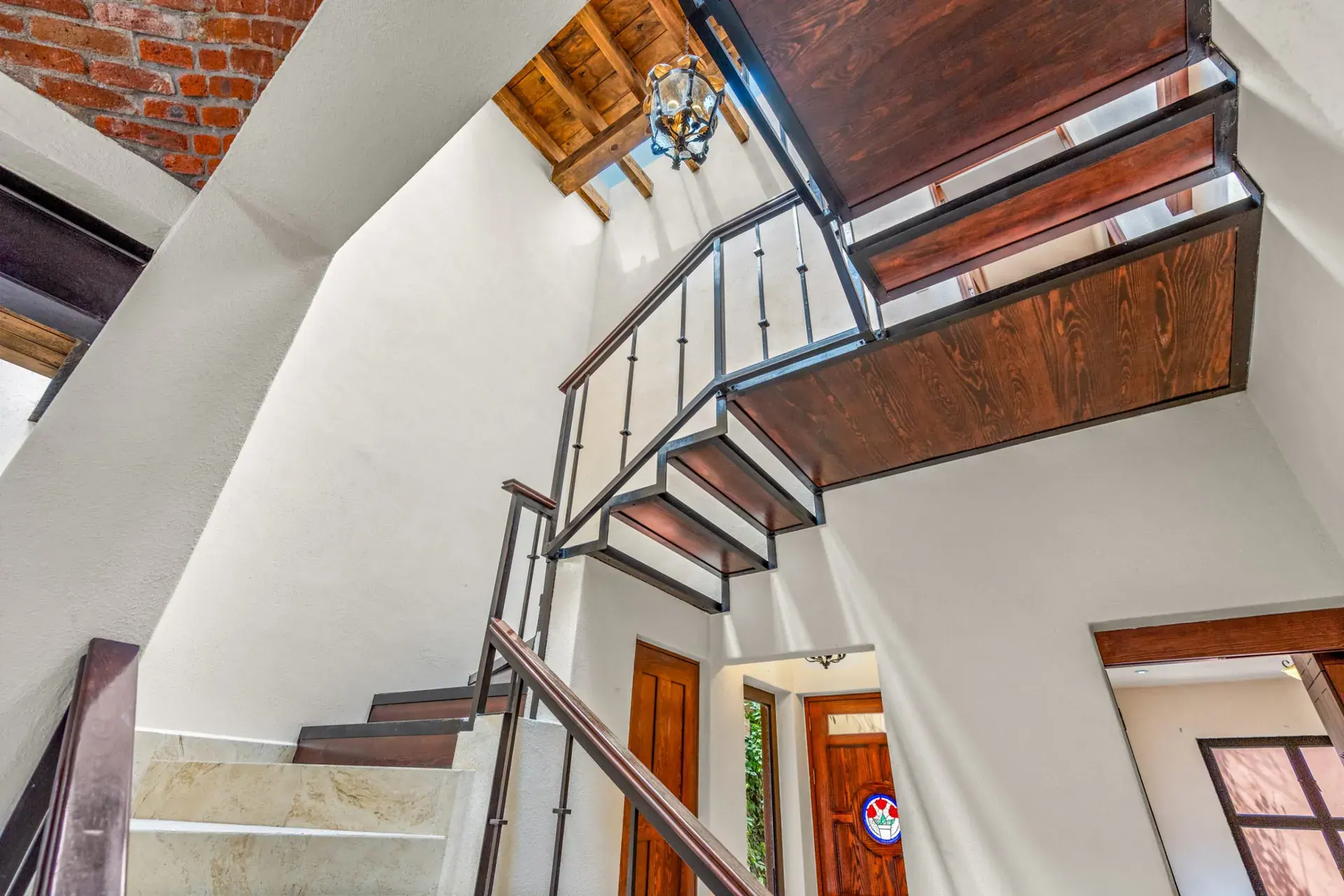 Casa Las Monjas, view looking up the steel and wood stairwell with a hanging lantern and brick wall, San Miguel de Allende