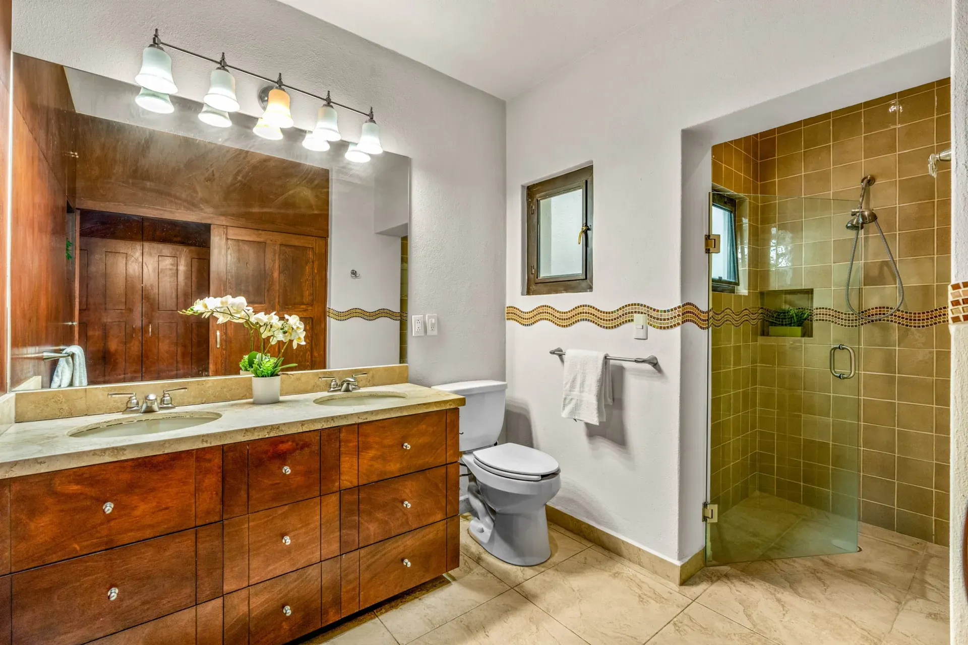 Casa Las Monjas, bathroom with a long wood double vanity, a large mirror and a glass shower with olive tile, San Miguel de Allende