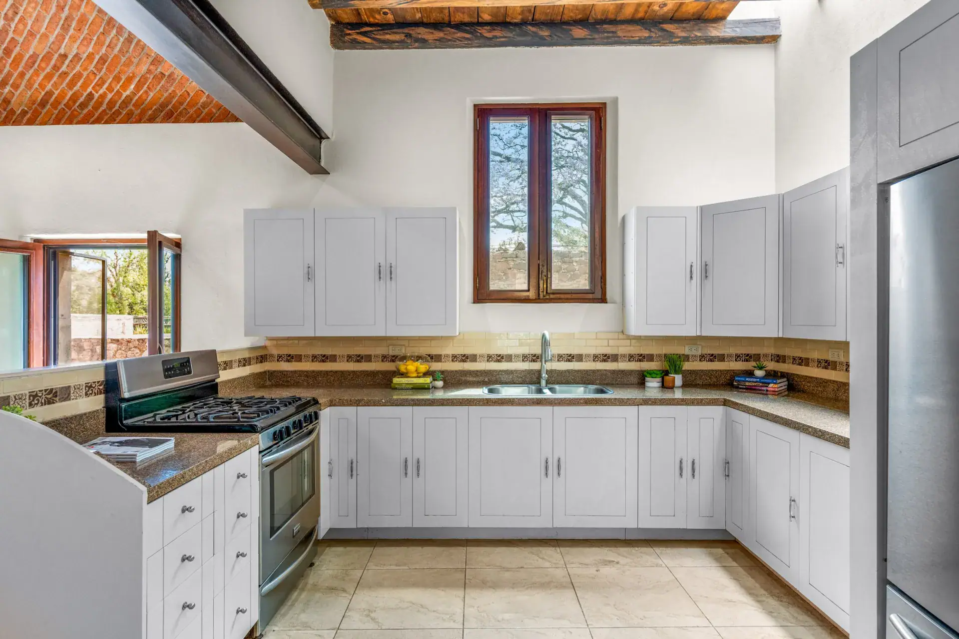 Casa Las Monjas, kitchen with white cabinets, a gas range, a stainless refrigerator and a window with wood frames under a brick vaulted ceiling, San Miguel de Allende