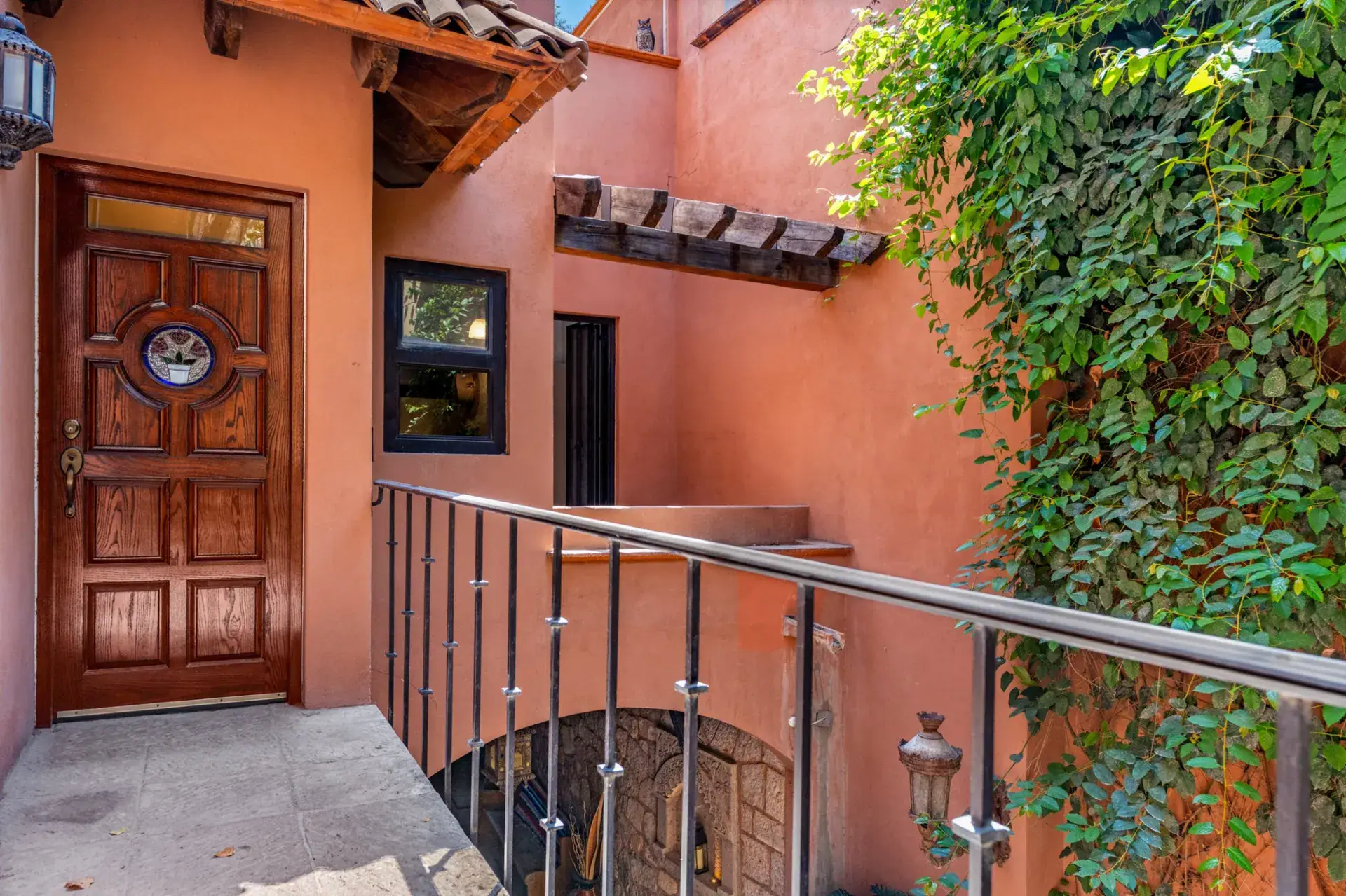 Casa Las Monjas, wood front door with a round window, a metal stair railing and climbing ivy on terracotta walls, San Miguel de Allende