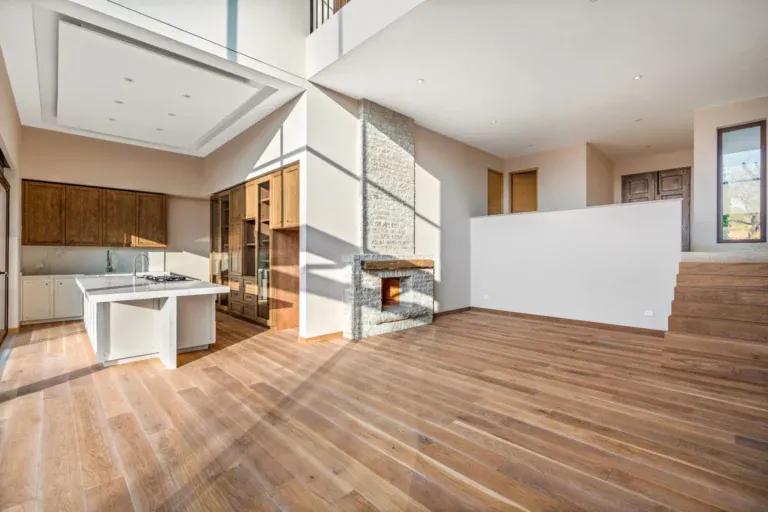 Casa Lavanda, empty open-plan main level with oak floors, a stone fireplace column and a kitchen island, with a mezzanine above, San Miguel de Allende