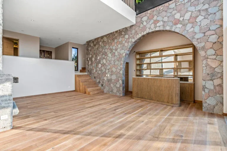 Casa Lavanda, open living space with a rough stone wall and arch, wood floors, a half wall and stairs to the upper level, San Miguel de Allende