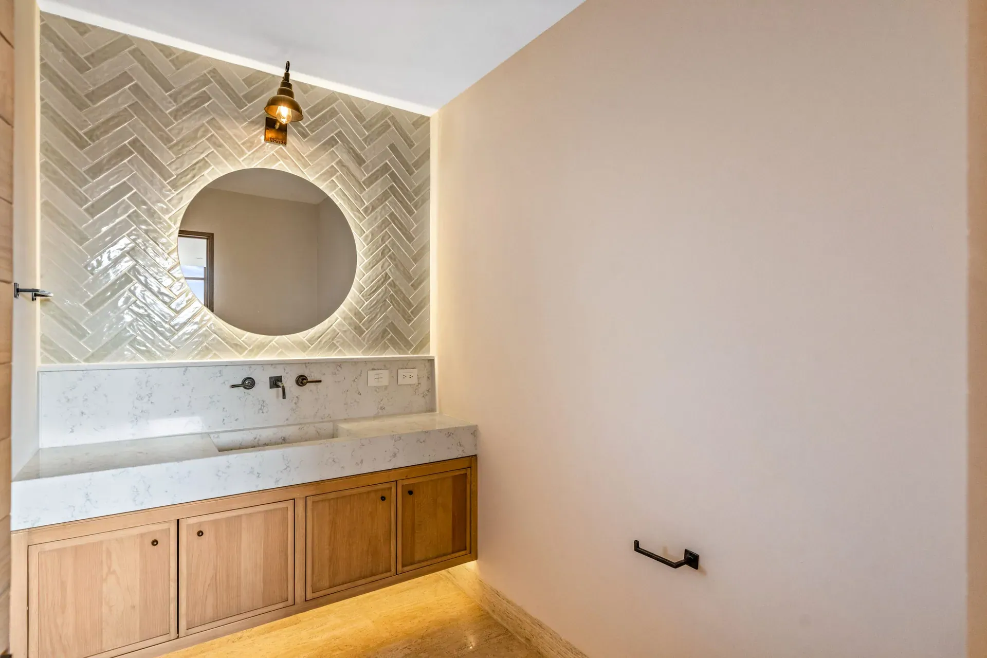 Casa Lavanda, bathroom with a herringbone tile wall, a round backlit mirror and a wood vanity under a quartz counter, San Miguel de Allende