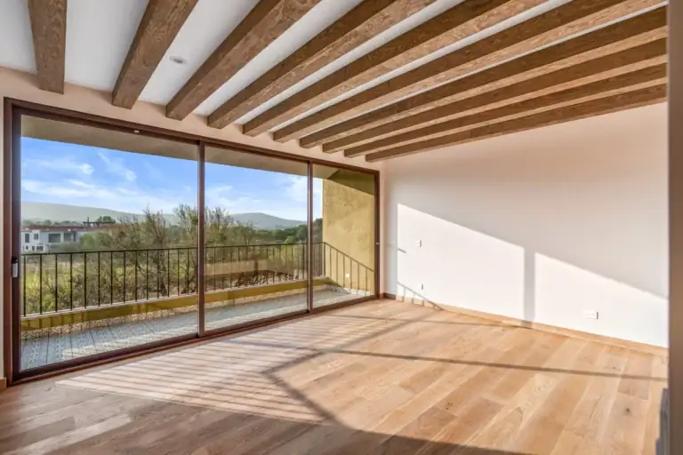Casa Lavanda, empty room with a wood-beam ceiling and a sliding glass wall onto a balcony with hills in view, San Miguel de Allende