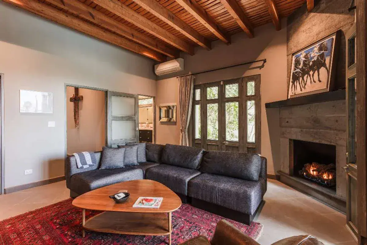 Casa Lily, living room with a dark leather sectional, a fireplace and a wood beam ceiling, San Miguel de Allende