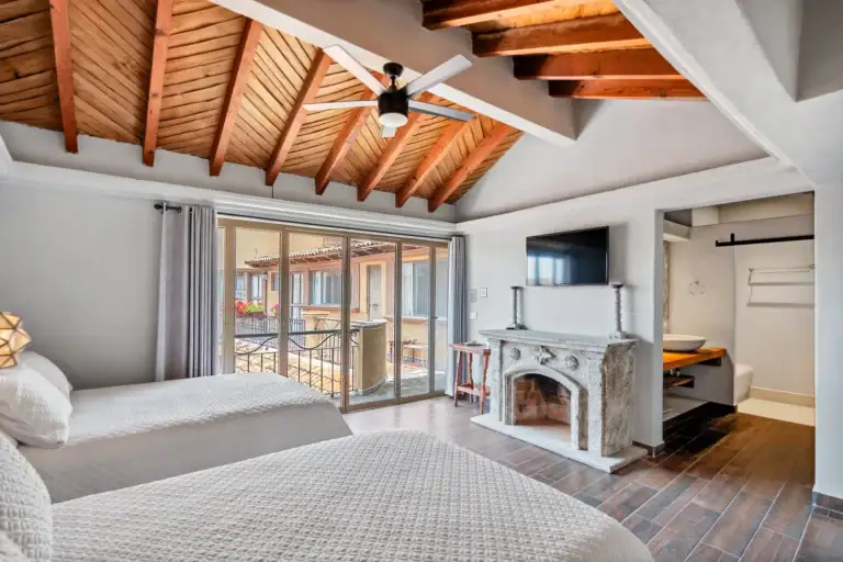 Casa Los Helechos, suite with a stone fireplace, twin beds, a wood-beam vaulted ceiling and sliding glass doors to a balcony, San Miguel de Allende