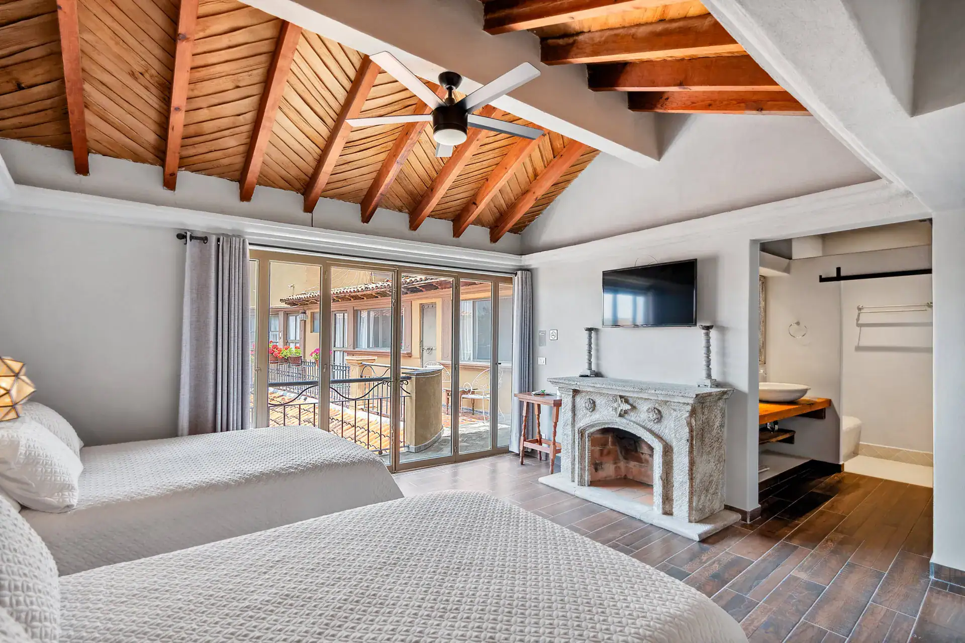 Casa Los Helechos, suite with a stone fireplace, twin beds, a wood-beam vaulted ceiling and sliding glass doors to a balcony, San Miguel de Allende