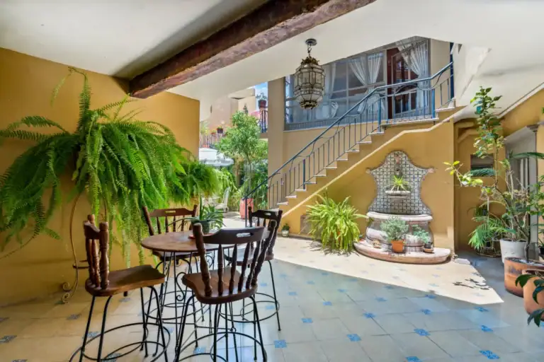 Casa Los Helechos, tiled courtyard with a bistro table, ferns, a tiled wall fountain and an iron staircase, San Miguel de Allende