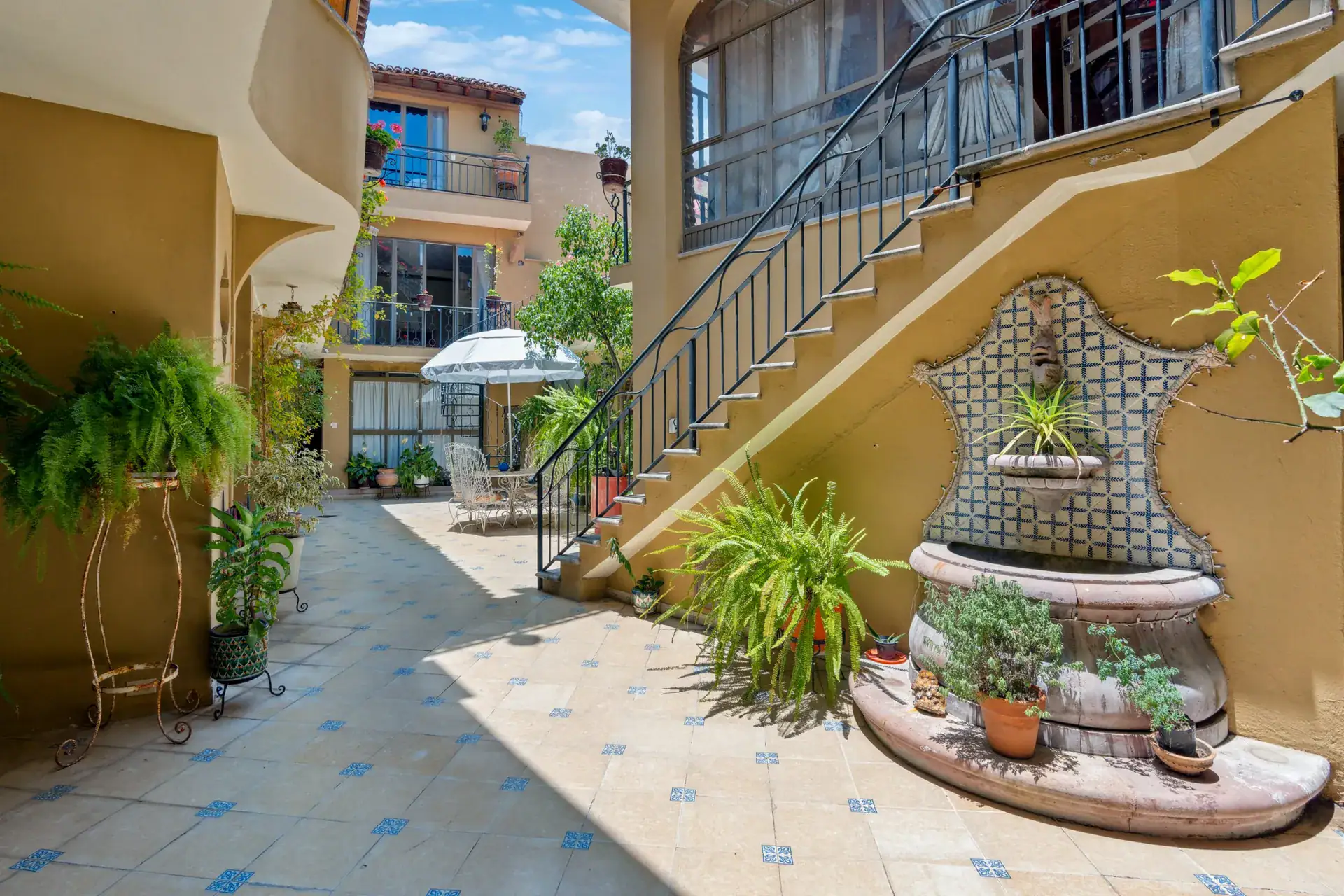 Casa Los Helechos, courtyard staircase with a blue iron railing and a tiled wall fountain with plants, San Miguel de Allende