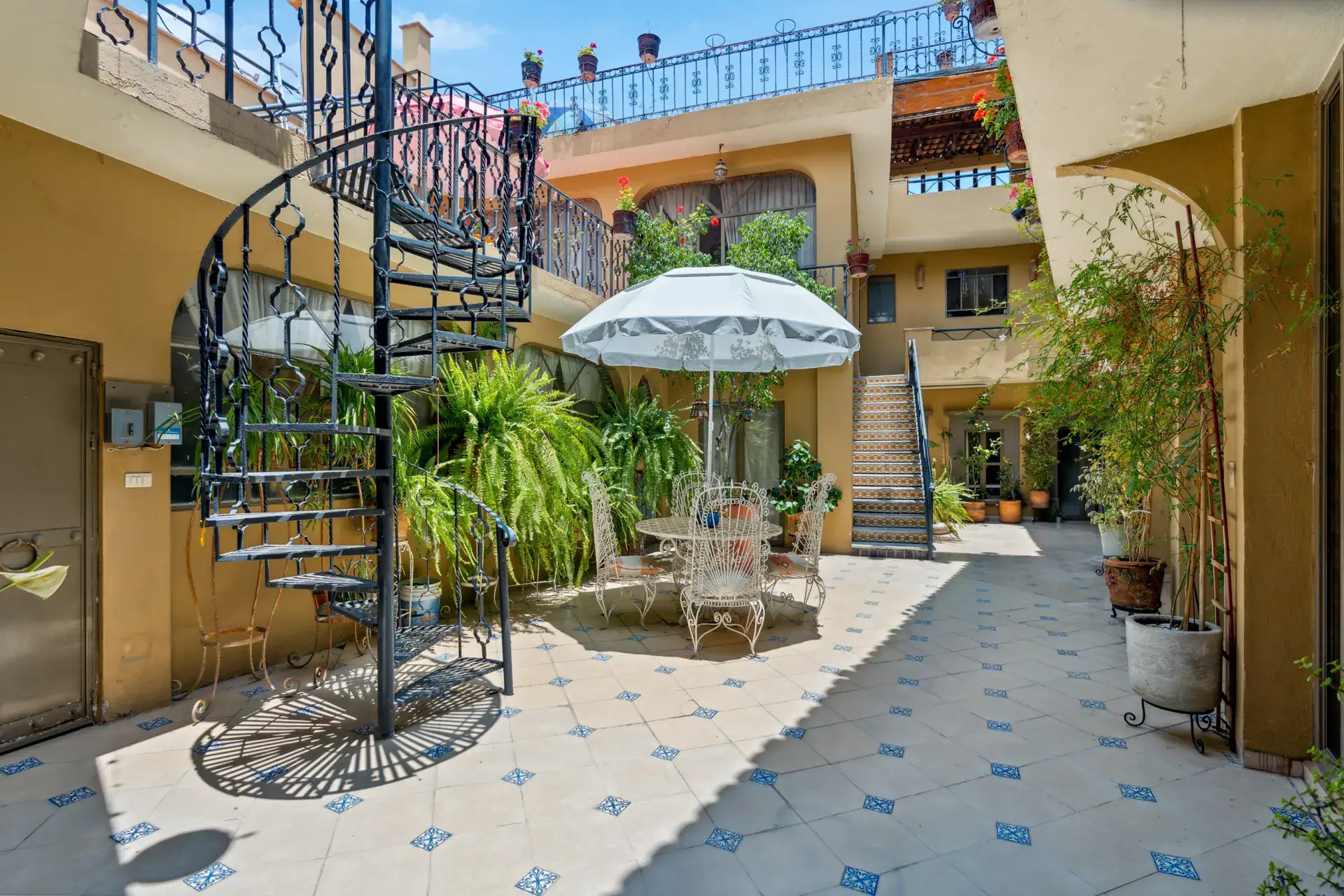 Casa Los Helechos, courtyard with a spiral iron staircase, a white umbrella and bamboo plants, San Miguel de Allende