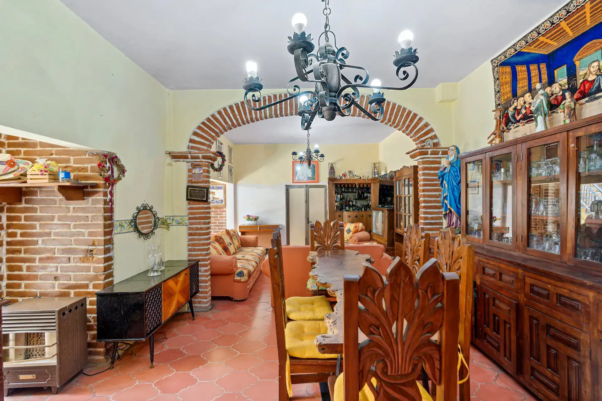 Casa Los Helechos, dining room with a carved wood table, an iron chandelier and a glass-front cabinet, San Miguel de Allende