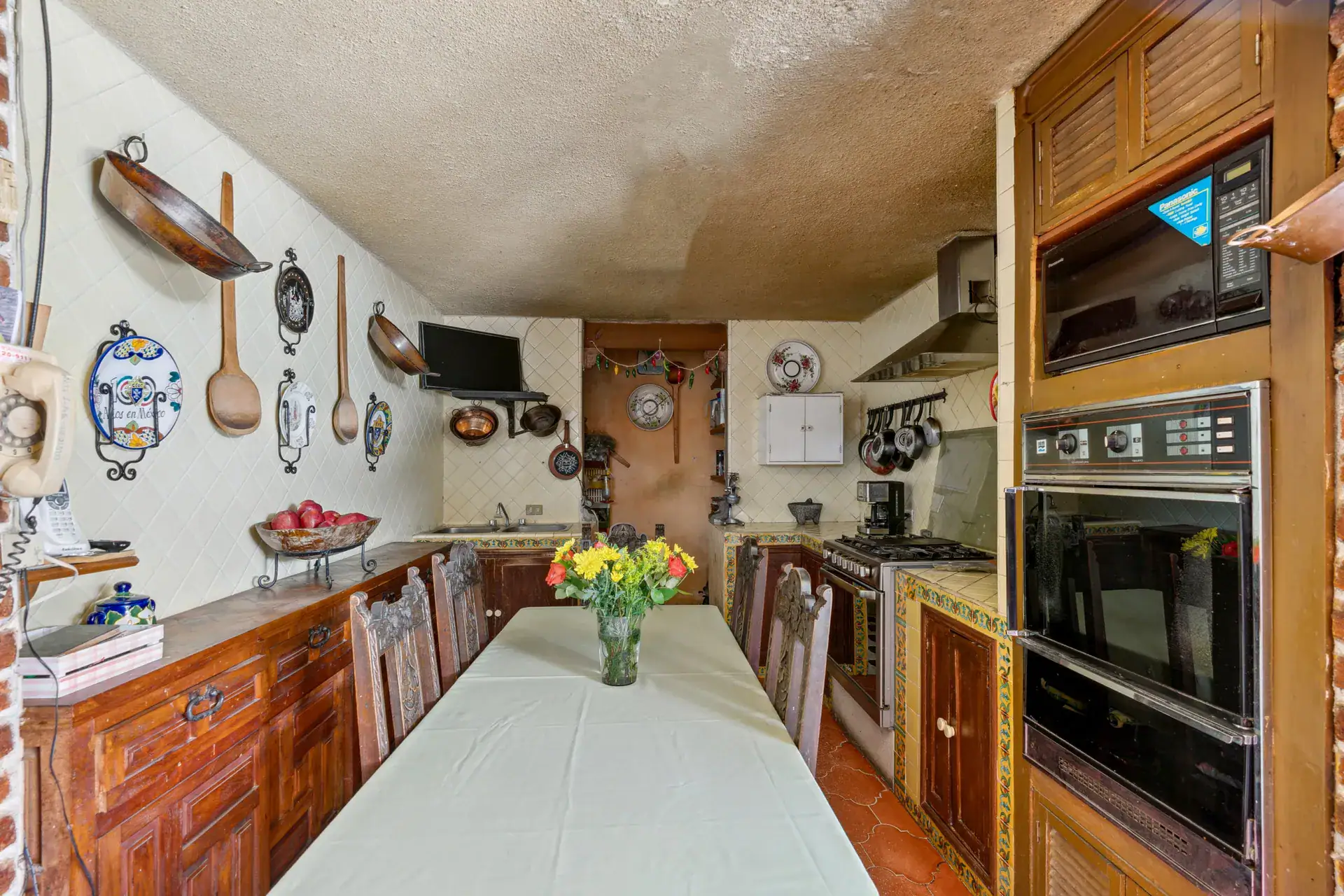 Casa Los Helechos, kitchen with a long table, wall-mounted pans and plates, a built-in oven and a wood cabinet, San Miguel de Allende