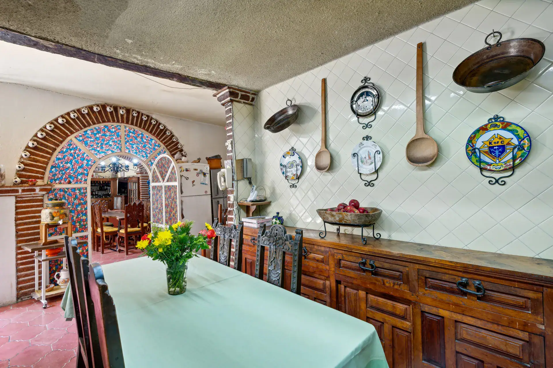 Casa Los Helechos, kitchen table with a mint tablecloth, a wooden sideboard and an arched tile mural, San Miguel de Allende