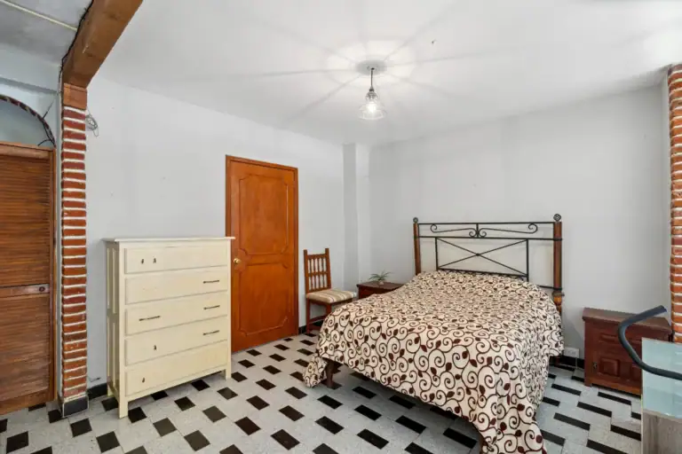 Casa Los Helechos, bedroom with an iron bed, a patterned bedspread, a white dresser and a checkered floor, San Miguel de Allende