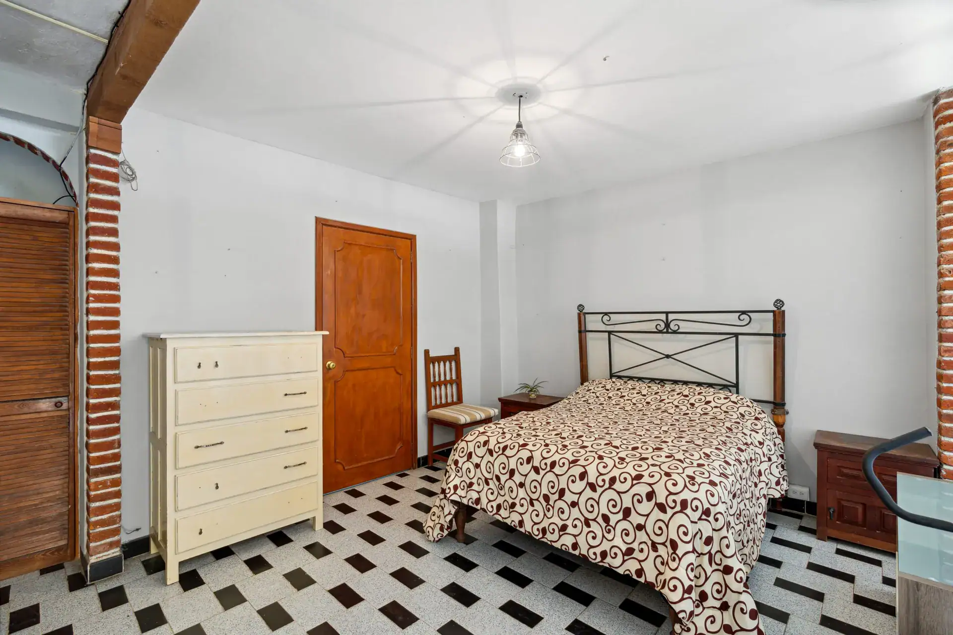Casa Los Helechos, bedroom with an iron bed, a patterned bedspread, a white dresser and a checkered floor, San Miguel de Allende