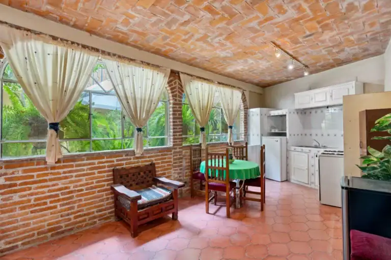 Casa Los Helechos, sunroom kitchenette with brick walls, curtained windows and a green-clothed table, San Miguel de Allende