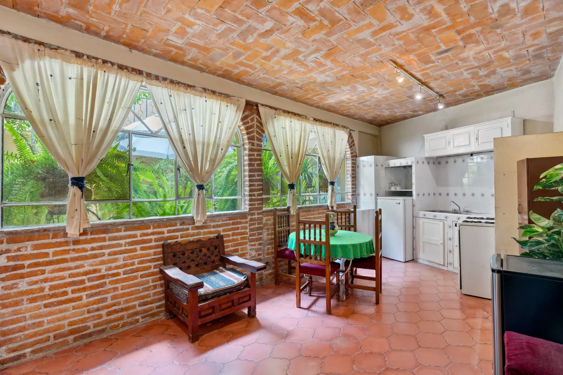 Casa Los Helechos, sunroom kitchenette with brick walls, curtained windows and a green-clothed table, San Miguel de Allende