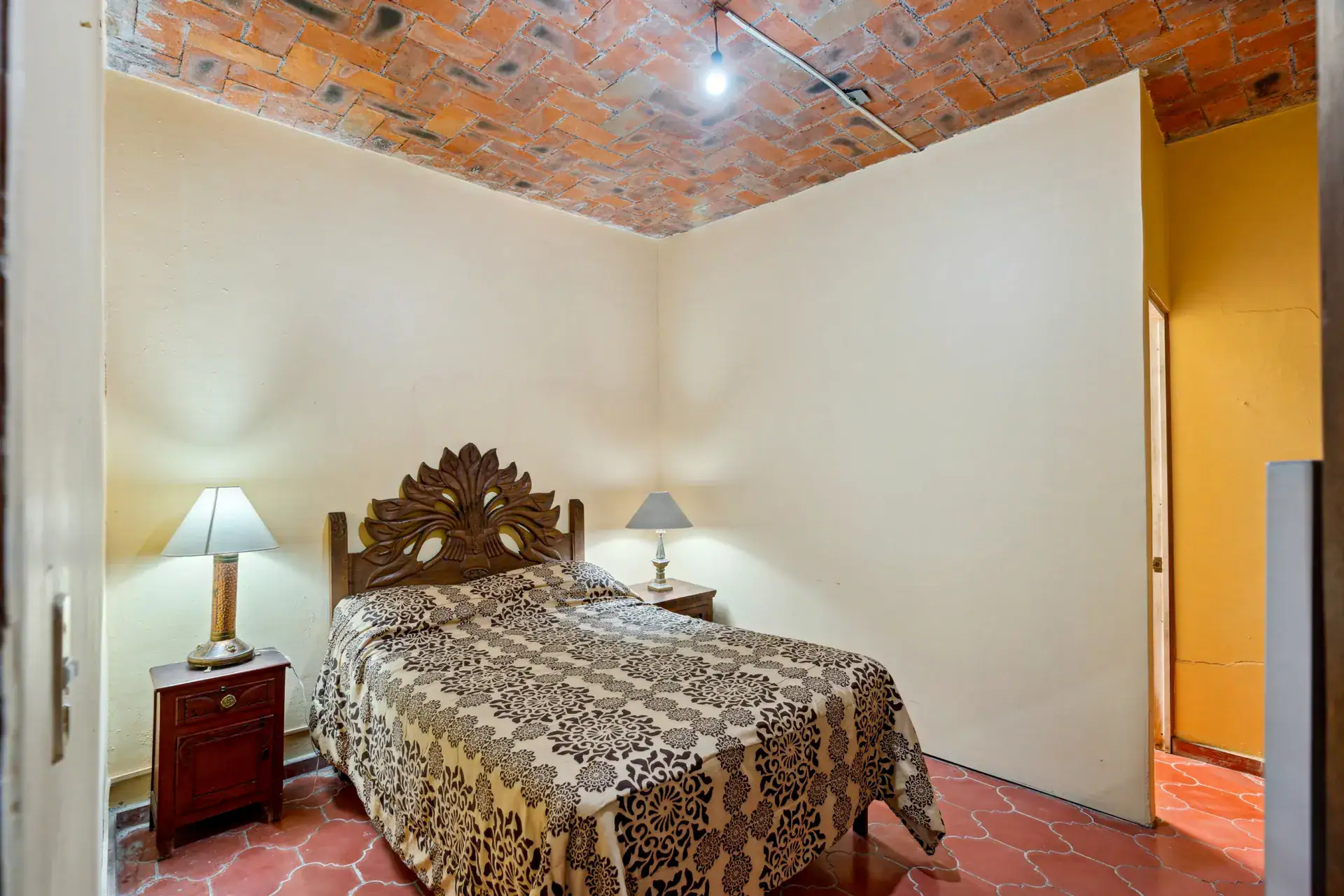 Casa Los Helechos, bedroom with a carved headboard, patterned bedspread and a brick ceiling, San Miguel de Allende