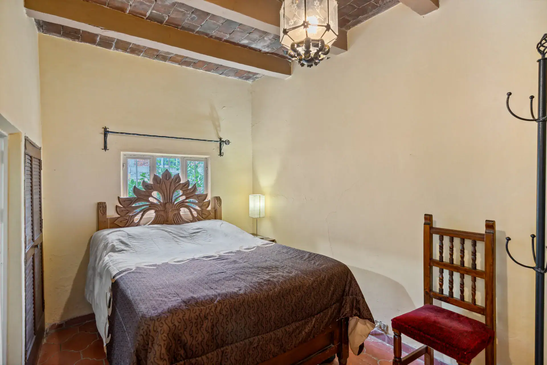 Casa Los Helechos, bedroom with a carved headboard, brown bedspread and a red-cushioned chair, San Miguel de Allende