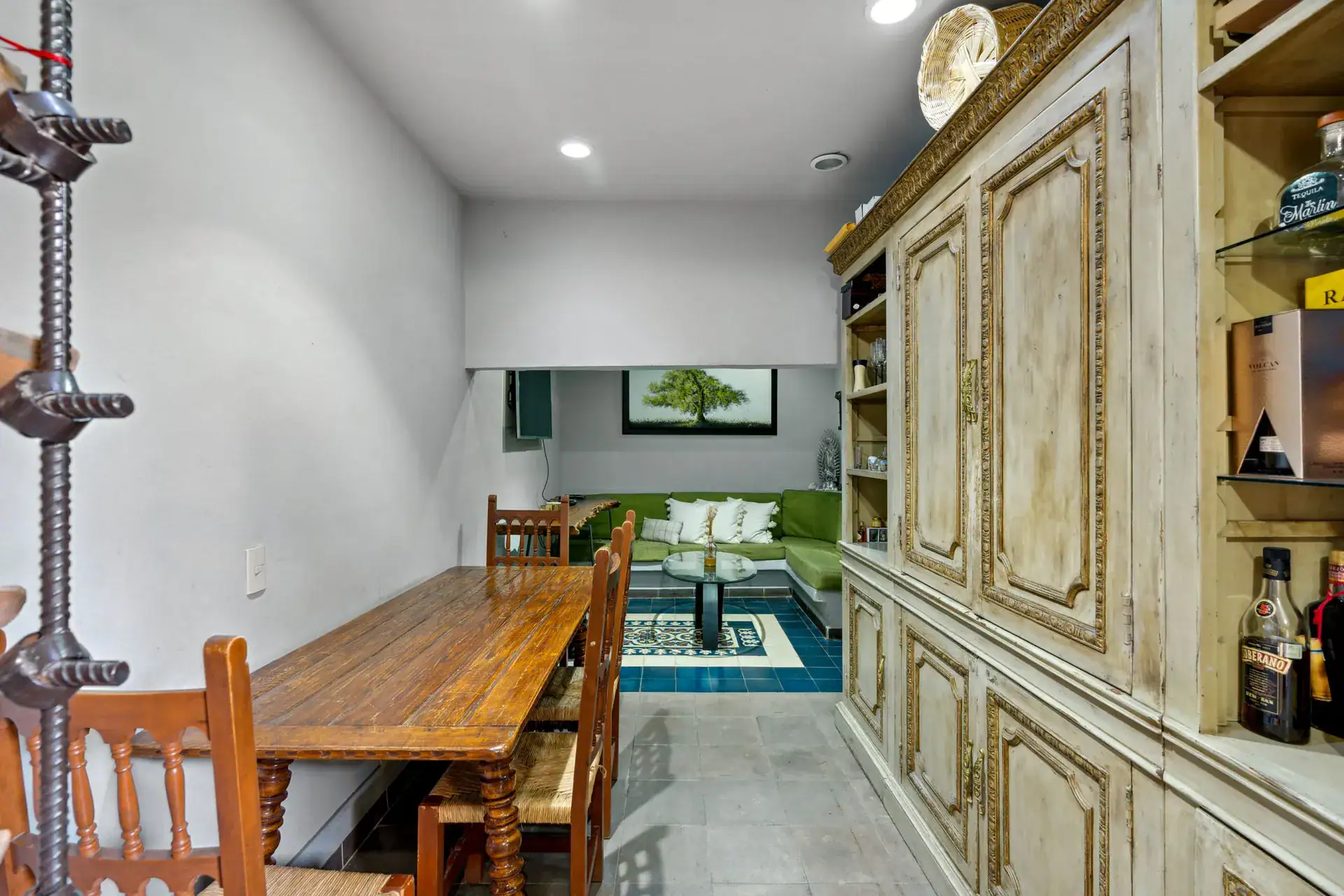 Casa Los Helechos, dining table with a view to a green sectional sofa in a lower lounge beside a carved cabinet wall, San Miguel de Allende