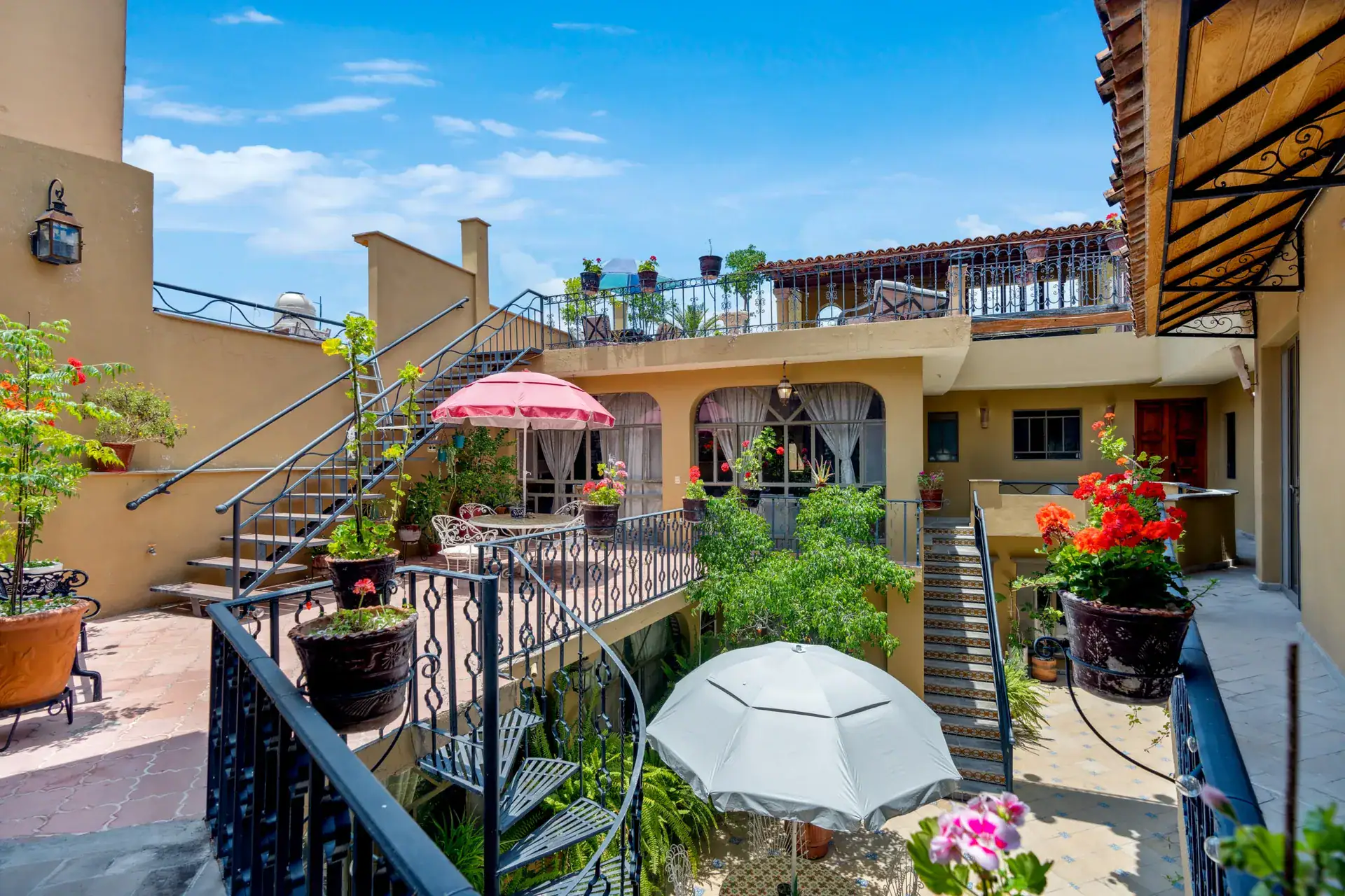 Casa Los Helechos, rooftop courtyard with red geranium pots, a pink umbrella and iron stairs, San Miguel de Allende