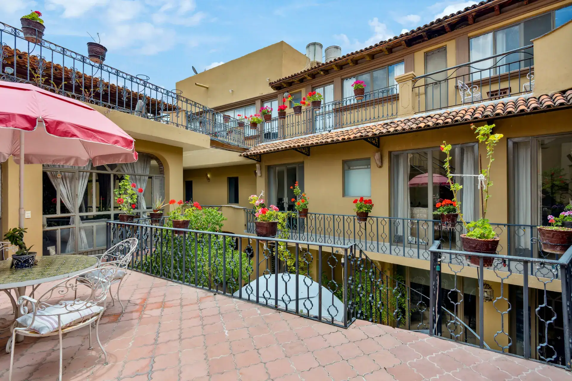 Casa Los Helechos, upper gallery terrace with a bistro set, iron railings and the multi-level courtyard, San Miguel de Allende