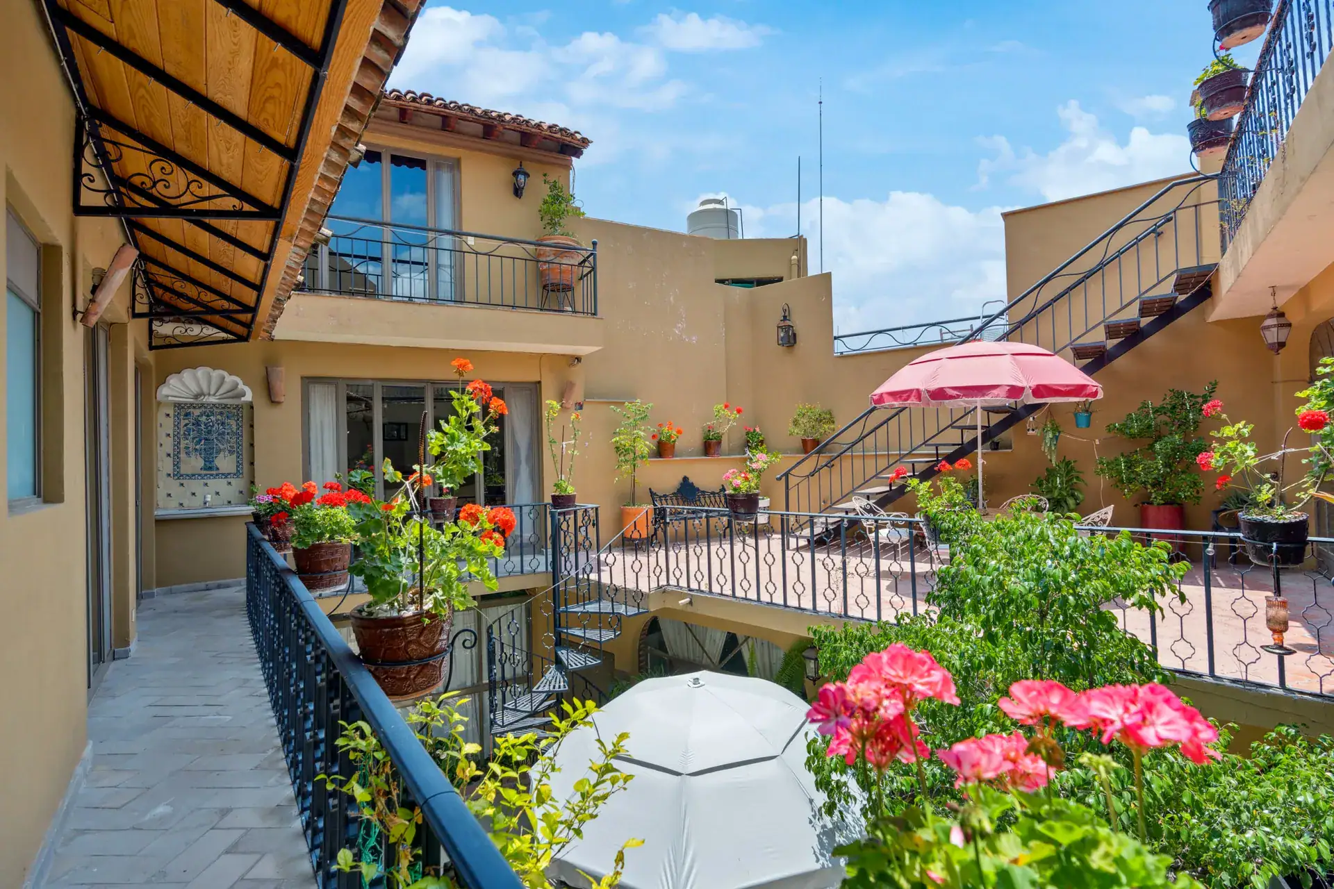 Casa Los Helechos, balcony walkway with a pink umbrella, red flowers and iron railings, San Miguel de Allende