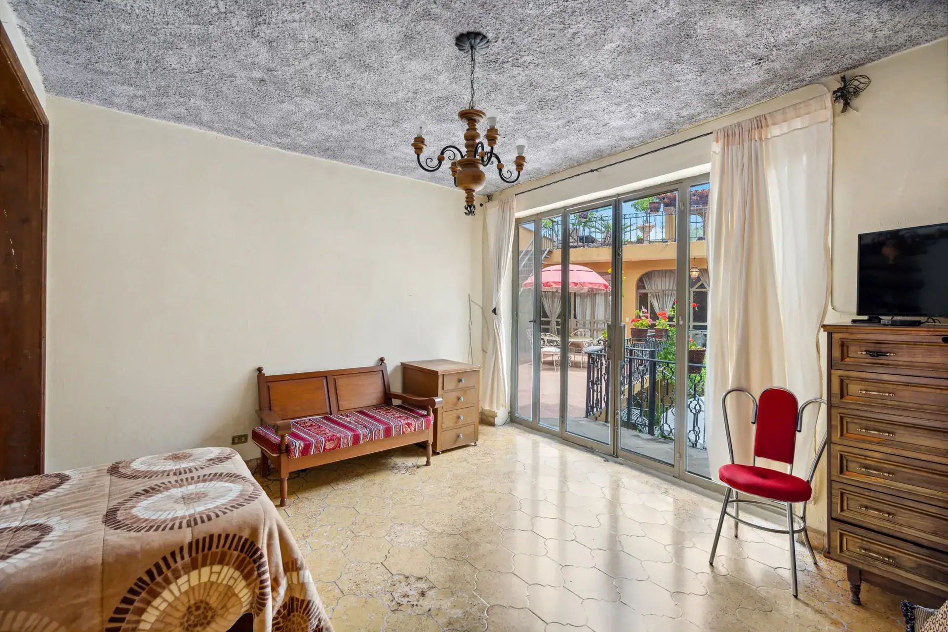 Casa Los Helechos, bedroom with a chandelier, sliding glass doors to the balcony and a patterned bench, San Miguel de Allende