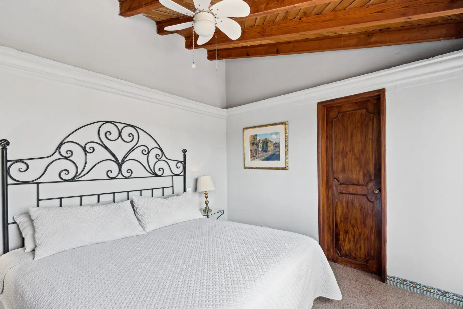 Casa Los Helechos, bedroom with an iron headboard, white bedding and a wood door, San Miguel de Allende