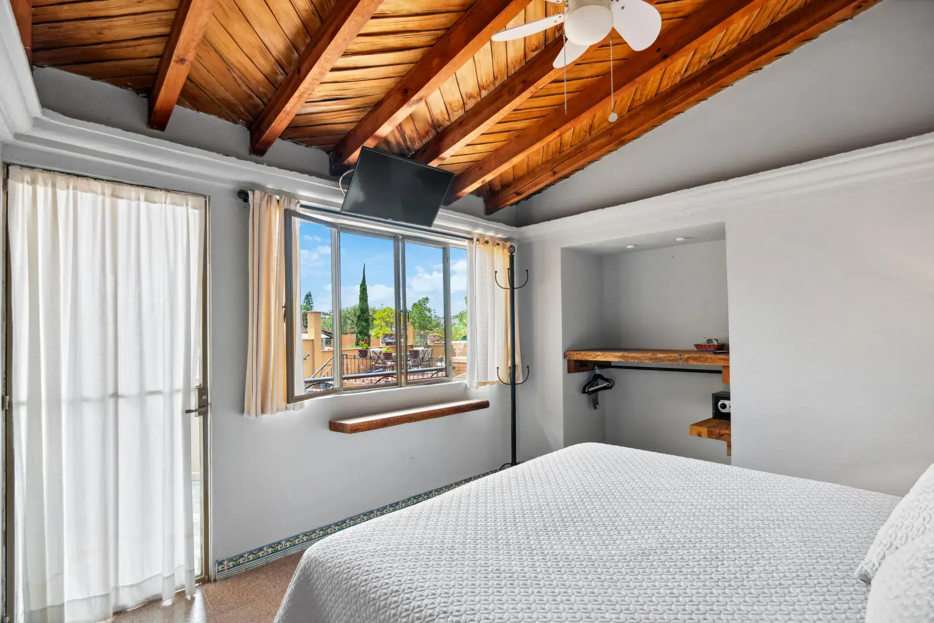 Casa Los Helechos, bedroom with a vaulted wood ceiling, white bedspread and a rooftop view, San Miguel de Allende